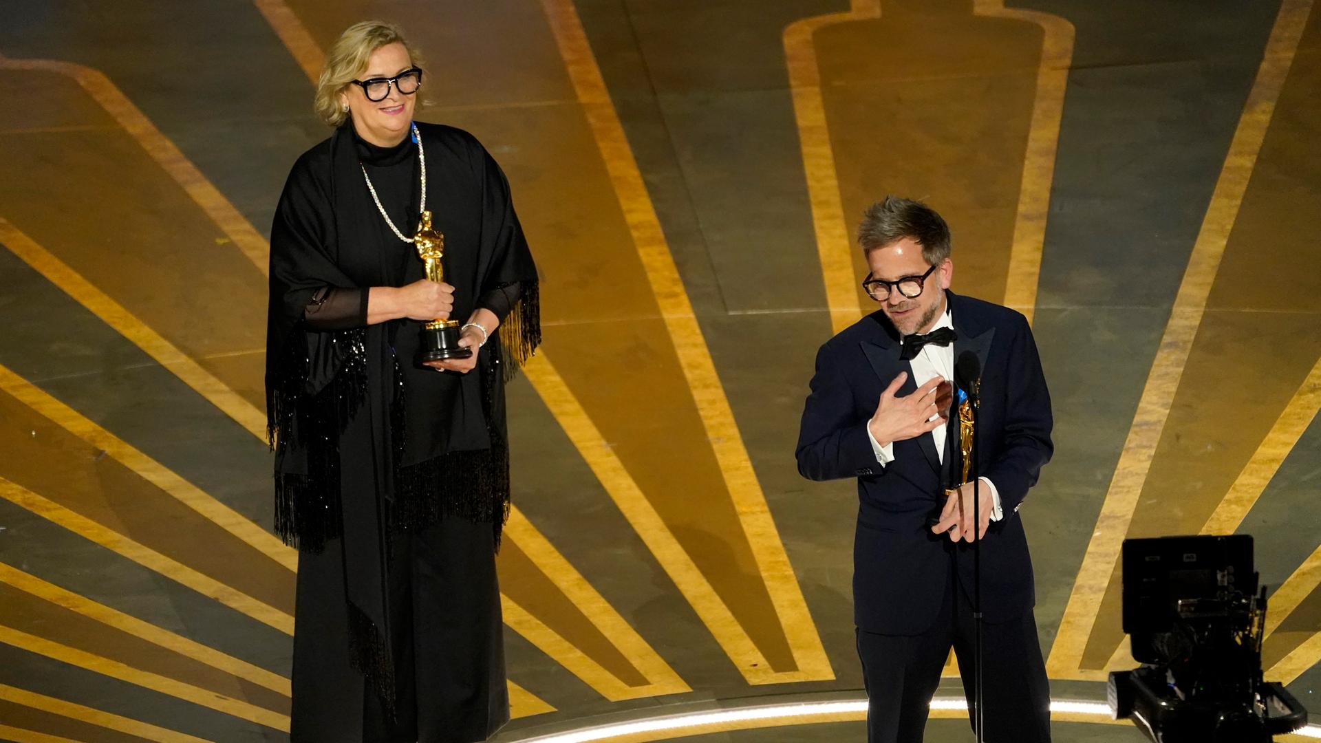 Ernestine Hipper im schwarzen Kleid und Christian M. Goldbeck im Smoking halten jeweils eine goldene Oscar-Statue in Händen.