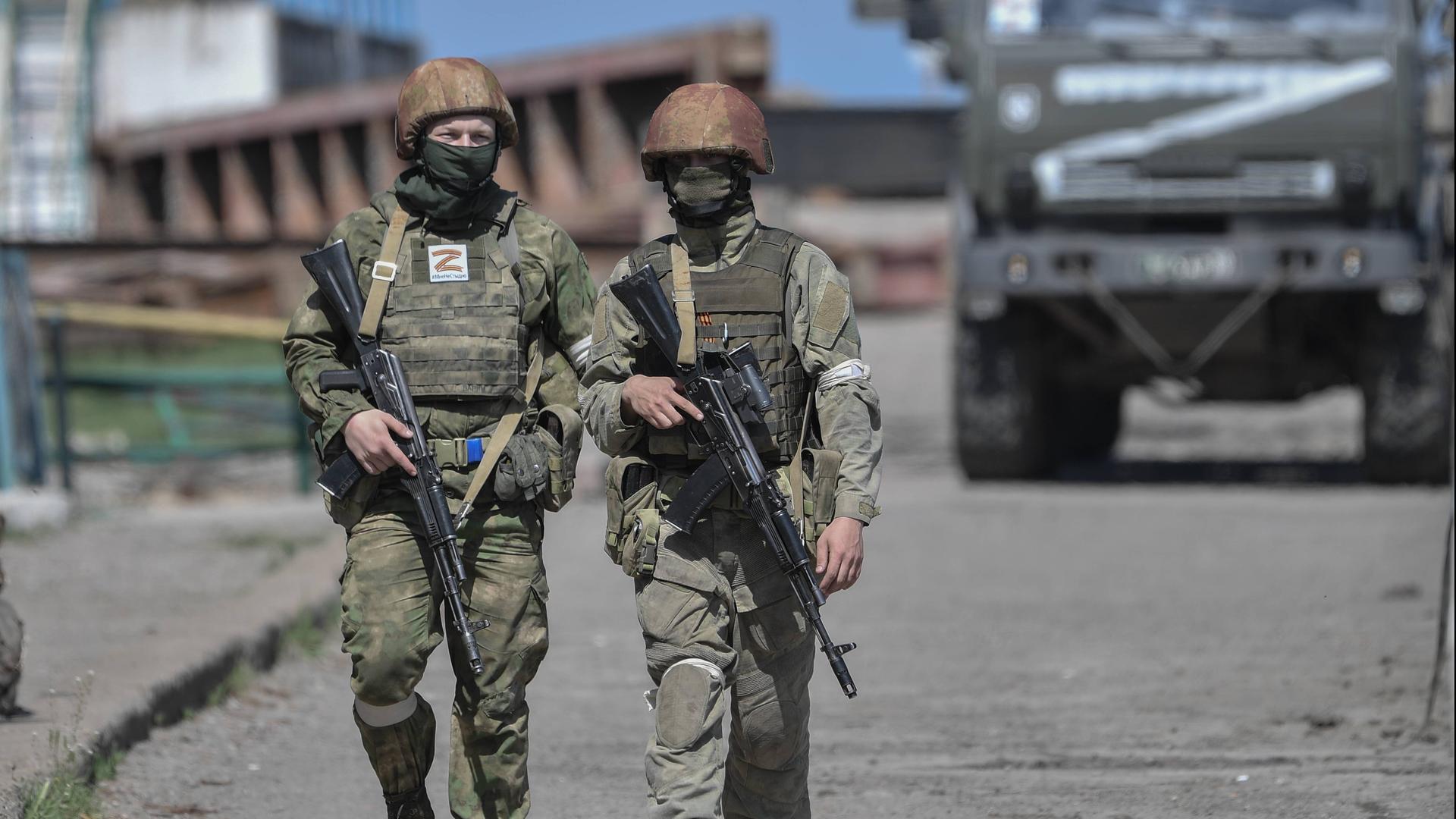 Zwei russische Soldaten in der Region Cherson, im Hintergrund ein Militärfahrzeug mit dem Z-Symbol.