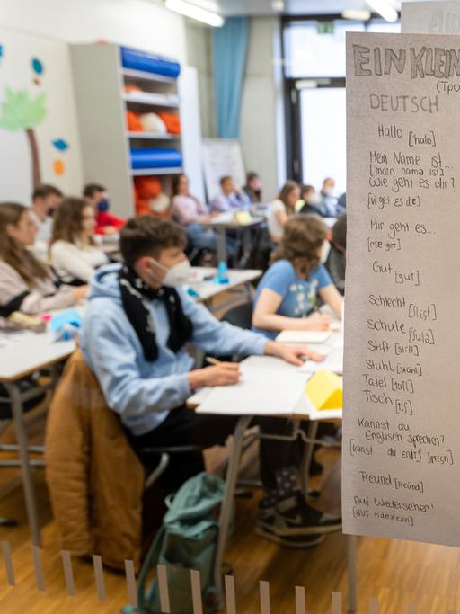 Kinder aus der Ukraine sitzen am Morgen in einer Willkommensklasse des Gymnasium Trudering. An einem Pfahl hängt ein Zettel mit einem WillkommensgruÃ auf Deutsch, Englisch und Ukrainisch.