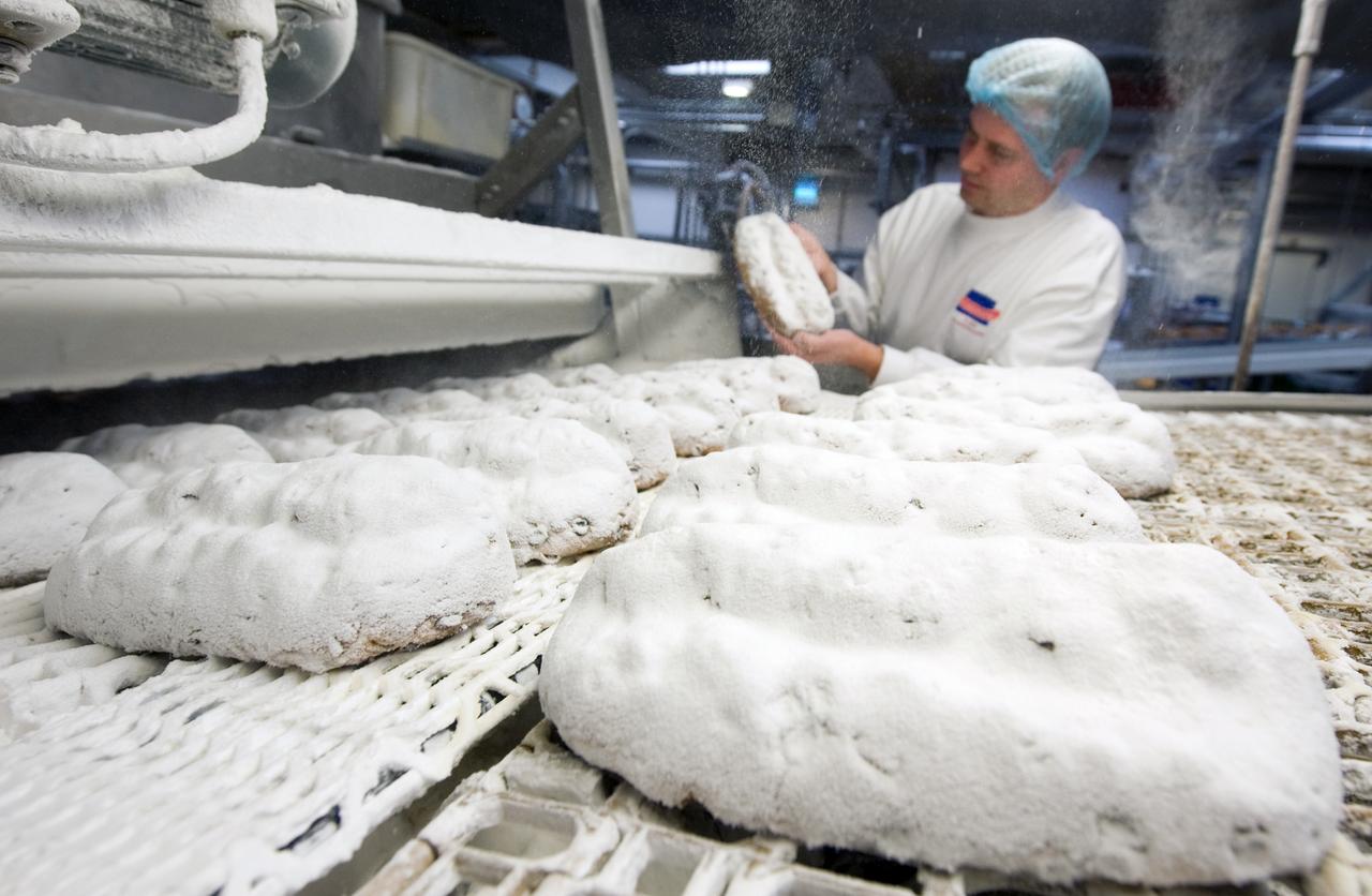 Christstollen werden bei Kuchenmeister in Soest gebacken. Ein Mann mit Haarschutz und in weißem Kittel kontrolliert einen der Stollen. Christstollen werden bei Kuchenmeister in Soest gebacken. Ein Mann mit Haarschutz und in weißem Kittel kontrolliert einen der Stollen.