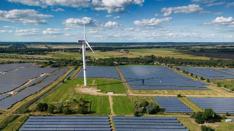 Eine Photovoltaik-Freiflächenanlage (Solarpark), betrieben von der Firma Enerparc. Zahlreiche Solarzellen in dem Solarkraftwerk wandeln Sonnenenergie in grünen Strom um. In dem Solarpark steht ein Windrad. (Luftaufnahme mit Drohne)