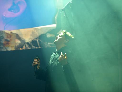 Kae Tempest steht bei einem Auftritt auf der Bühne, hat die Augen geschlossen und den Kopf nach oben gedreht, in Richtung eines grünen Lichtstrahls von der Decke.