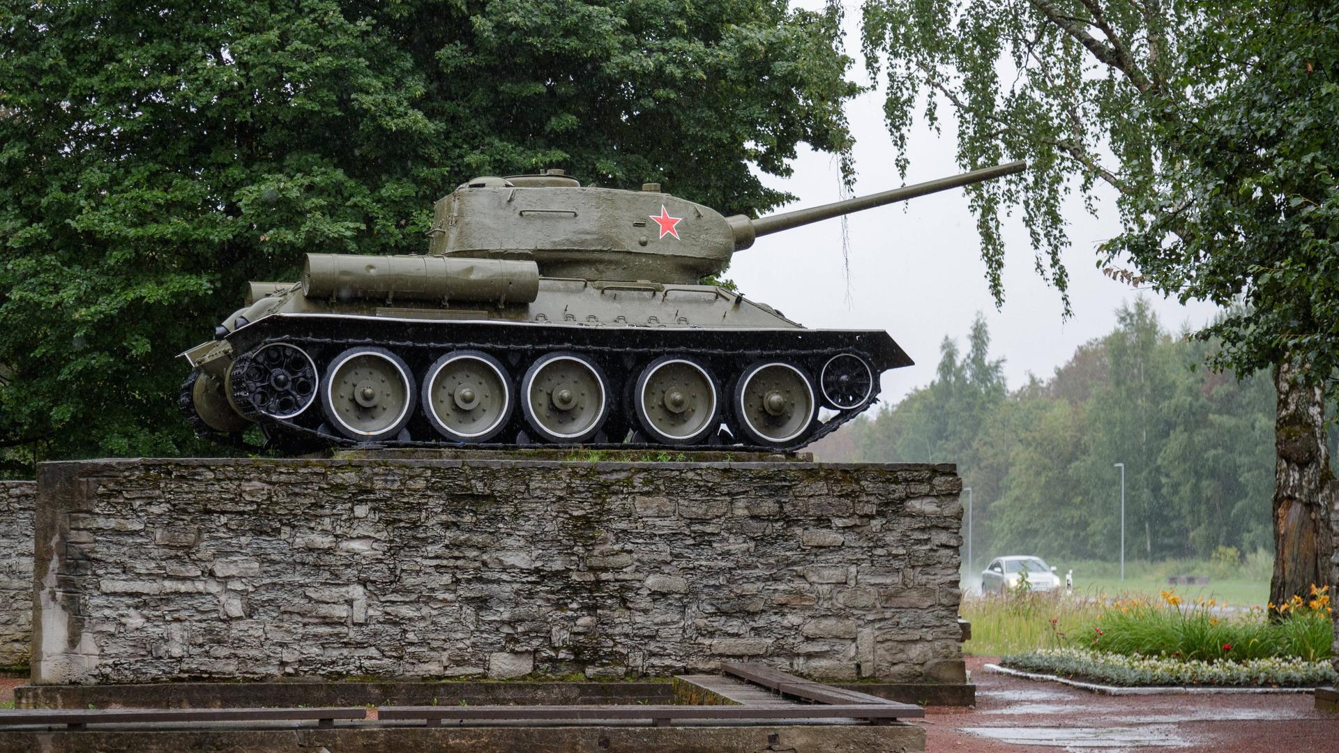 Ein historischer Sowjetpanzer steht im estnischen Narva auf einem Steinsockel, im Hintergrund sind Bäume zu sehen.