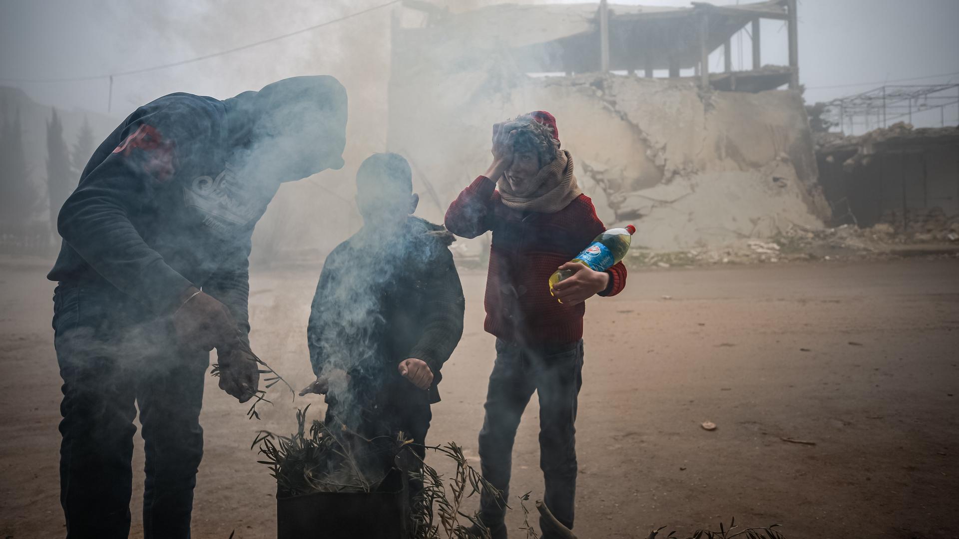 Drei Menschen verbrennen Müll in einer Feuertonne, um sich zu wärmen, in Idlib, Syrien. Drei Menschen verbrennen Müll in einer Feuertonne, um sich zu wärmen, in Idlib, Syrien.