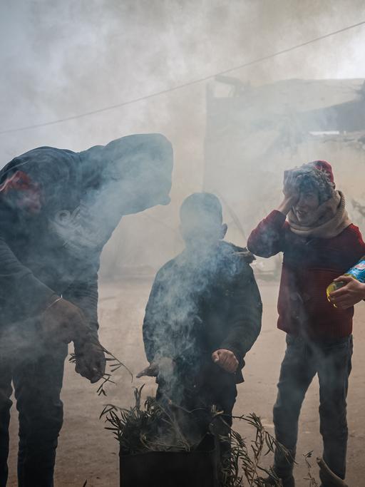 Drei Menschen verbrennen Müll in einer Feuertonne, um sich zu wärmen, in Idlib, Syrien.