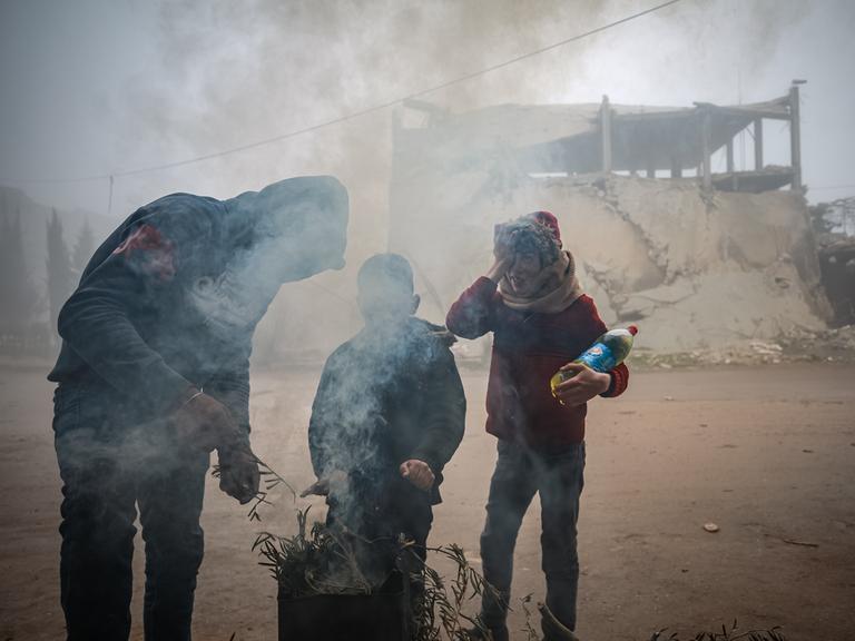Drei Menschen verbrennen Müll in einer Feuertonne, um sich zu wärmen, in Idlib, Syrien.