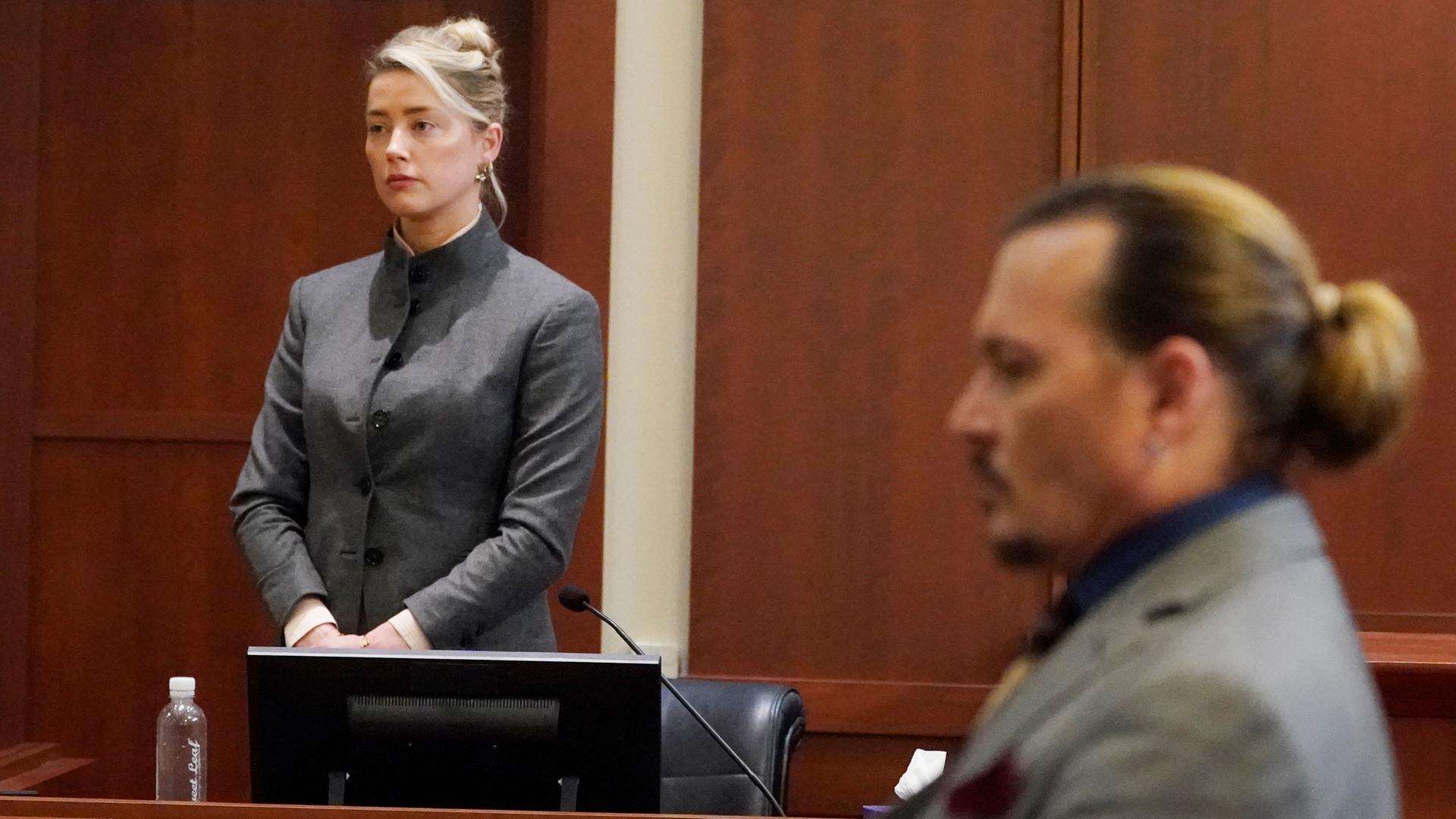 Amber Heard stehend bei einer Aussage im Gerichtssaal, im Vordergrund hört ihr Ex-Ehemann Johnny Depp zu. Amber Heard stehend bei einer Aussage im Gerichtssaal, im Vordergrund hört ihr Ex-Ehemann Johnny Depp zu.