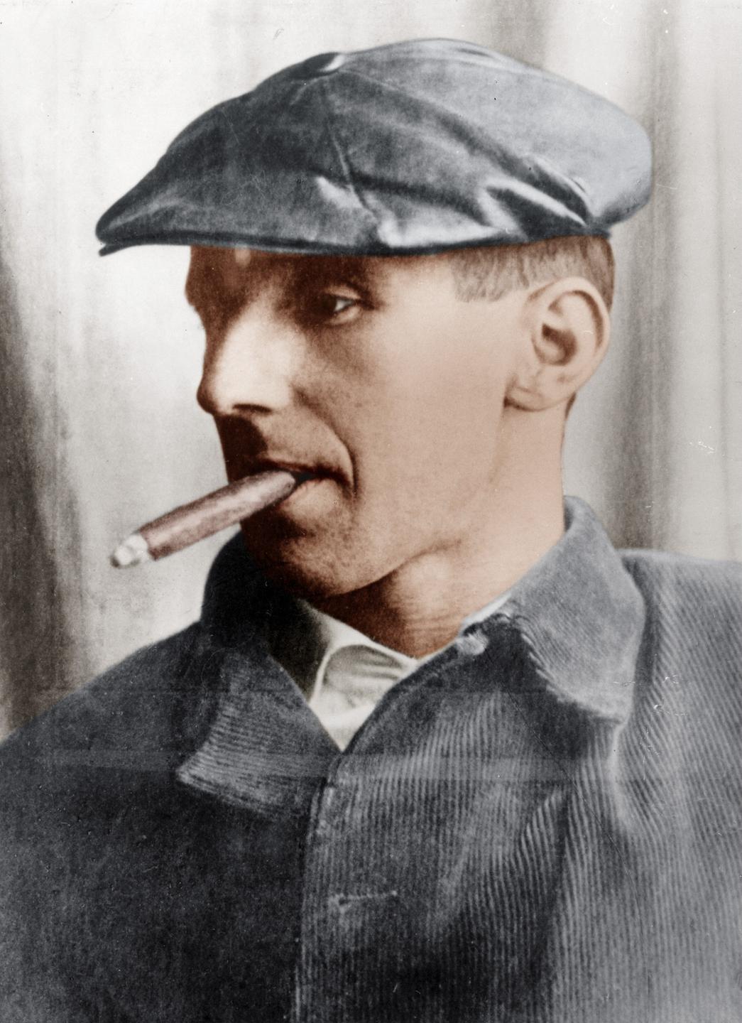 Nachkoloriertes Portrait von Bertolt Brecht mit Schiebermütze und Zigarre um 1931.