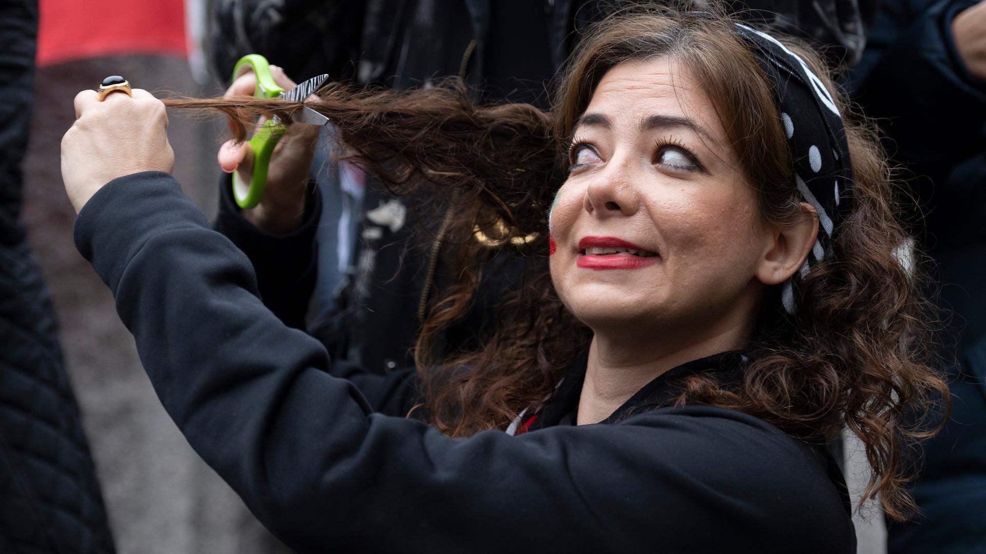 Eine Frau hält sich ein Schere an eine Strähne ihres Haares - Solidaritätsgeste für die Proteste im Iran auf einer Demo in Washington. Eine Frau hält sich ein Schere an eine Strähne ihres Haares - Solidaritätsgeste für die Proteste im Iran auf einer Demo in Washington.