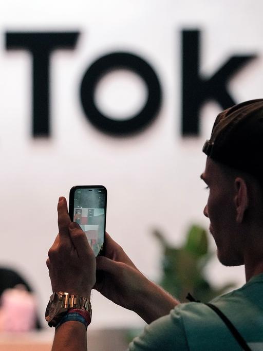 Ein Besucher der Messe Gamescom macht mit dem Smartphone ein Foto vom TikTok-Stand.