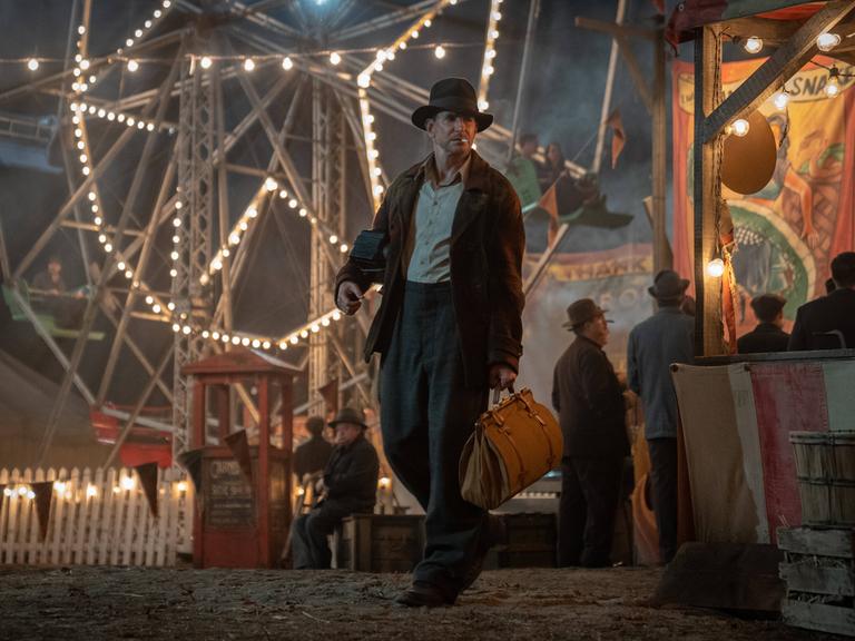 In dem Film Nightmare Alley von Regisseur Guillermo del Toro geht der von Bradley Cooper gespielte Betrüger Stan Carlisle über einen von einem Riesenrad erleuchteten Jahrmarkt.