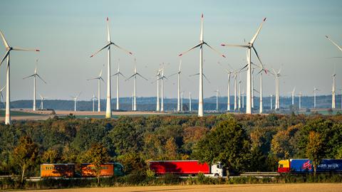 Eine Reihe von Windrädern hinter einer Autobahn, auf der Lkws fahren.