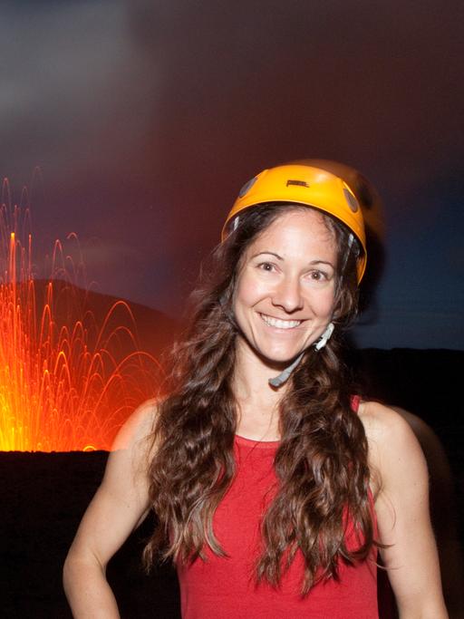 Die Fotografin Ulla Lohmann mit Helm auf dem Vulkan Yasur in Vanuatu mit Feuer im Hintergrund. 