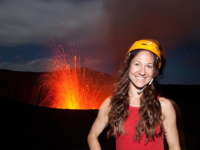 Die Fotografin Ulla Lohmann mit Helm auf dem Vulkan Yasur in Vanuatu mit Feuer im Hintergrund. 