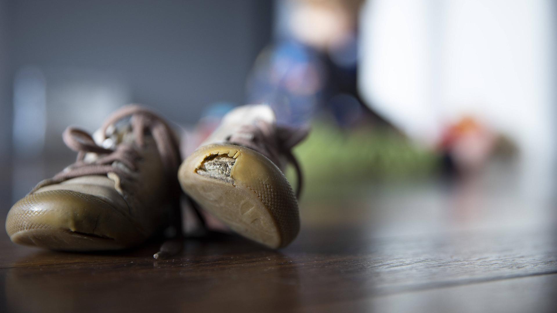 Ein paar Kinderschuhe, wobei der linke Schuh eine großes Loch hat. Ein paar Kinderschuhe, wobei der linke Schuh eine großes Loch hat.