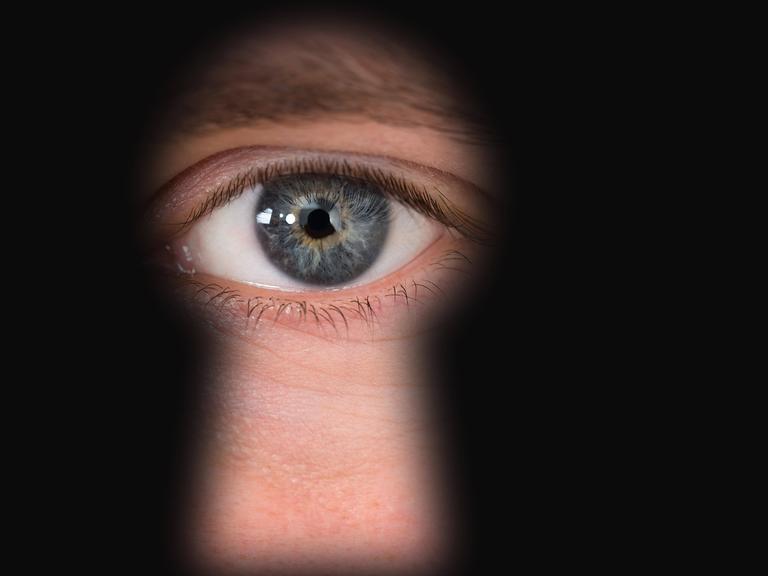 Ein blau-graues Auge ist durch ein Schlüsselloch zu sehen.