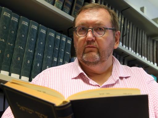Walter Homolka mit einem Buch in der Hand, vor einem Buchregal