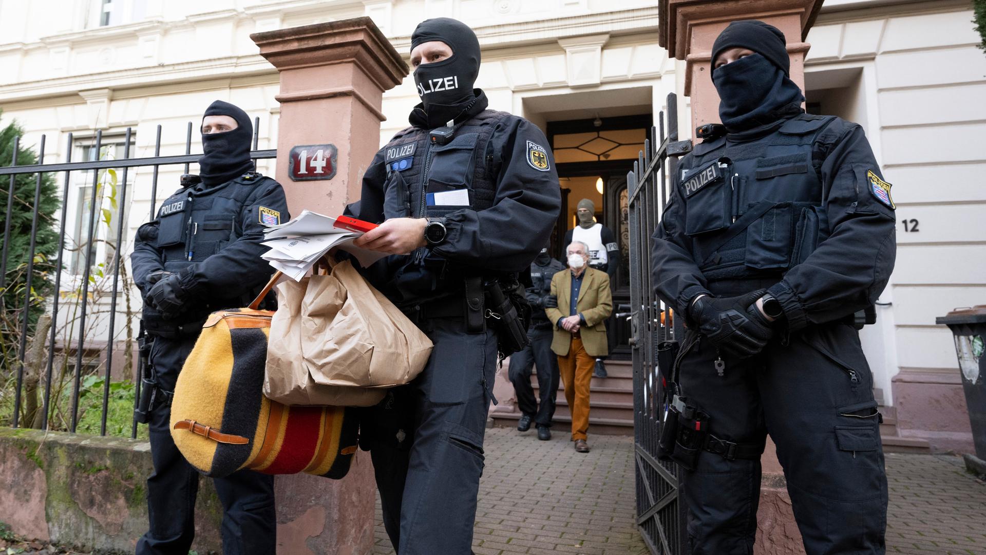 Bei einer Razzia gegen sogenannte "Reichsbürger" führen vermummte Polizisten nach der Durchsuchung eines Hauses Heinrich XIII Prinz Reuß (hinten, Mitte) zu einem Polizeifahrzeug. Ein Polizist trägt dabei Tüten, eine Tasche und Papiere. Bei einer Razzia gegen sogenannte "Reichsbürger" führen vermummte Polizisten nach der Durchsuchung eines Hauses Heinrich XIII Prinz Reuß (hinten, Mitte) zu einem Polizeifahrzeug. Ein Polizist trägt dabei Tüten, eine Tasche und Papiere.