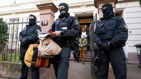 Bei einer Razzia gegen sogenannte "Reichsbürger" führen vermummte Polizisten nach der Durchsuchung eines Hauses Heinrich XIII Prinz Reuß (hinten, Mitte) zu einem Polizeifahrzeug. Ein Polizist trägt dabei Tüten, eine Tasche und Papiere. 