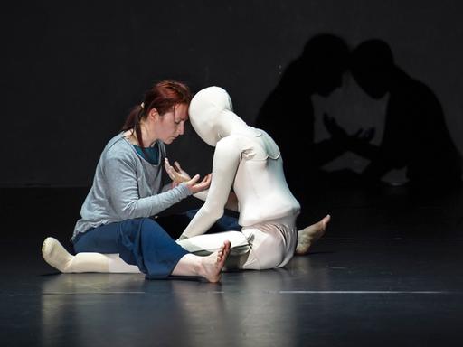 Szene im Theaterstück "Schattenkind", auf der Bühne ganz in schwarz gehalten umarmen sich die Protagonistin und eine weiße, lebensgroßen Puppe.