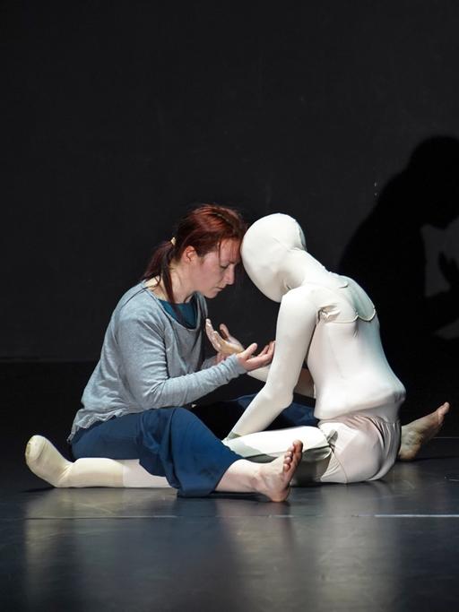 Szene im Theaterstück "Schattenkind", auf der Bühne ganz in schwarz gehalten umarmen sich die Protagonistin und eine weiße, lebensgroßen Puppe.