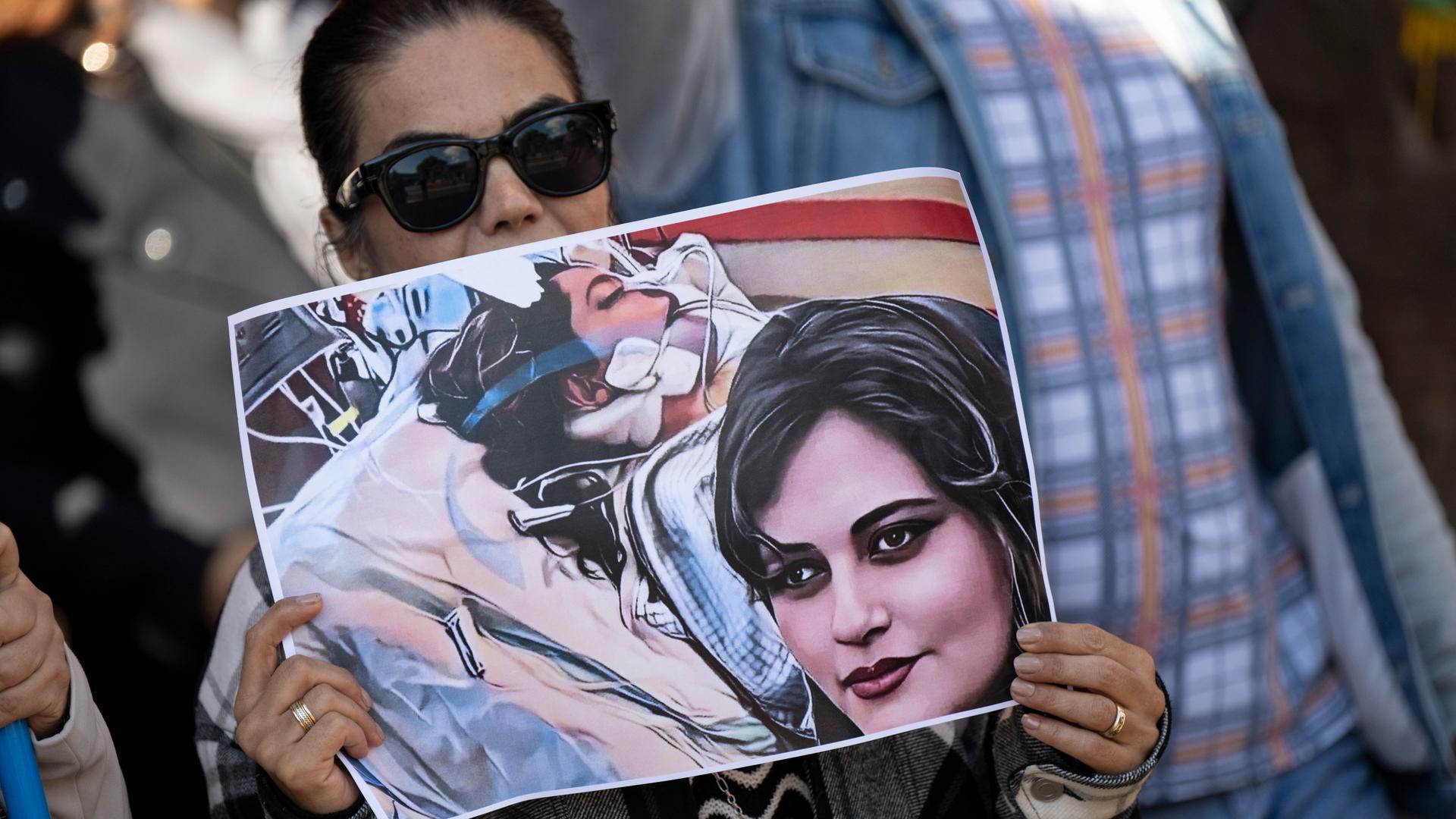 Eine Iranerin beteiligt sich vor dem US-Konsulat in Frankfurt an einer Demonstration gegen das Regime im Iran. Dabei hält sie ein Plakat mit dem Bild der 22-jährigen Mahsa Amini in den Händen. Eine Iranerin beteiligt sich vor dem US-Konsulat in Frankfurt an einer Demonstration gegen das Regime im Iran. Dabei hält sie ein Plakat mit dem Bild der 22-jährigen Mahsa Amini in den Händen.