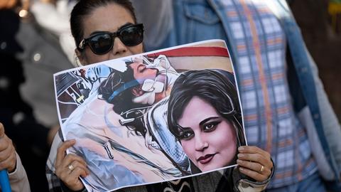 Eine Iranerin beteiligt sich vor dem US-Konsulat in Frankfurt an einer Demonstration gegen das Regime im Iran. Dabei hält sie ein Plakat mit dem Bild der 22-jährigen Mahsa Amini in den Händen.