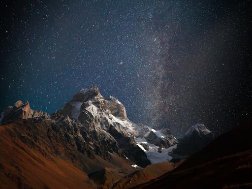 Nächtlicher Blick auf den Berg Ushba mit dunklem Sternenhimmel im Kaukasusgebirge.