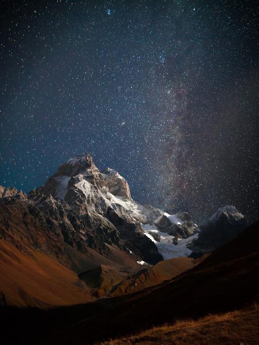 Nächtlicher Blick auf den Berg Ushba mit dunklem Sternenhimmel im Kaukasusgebirge.