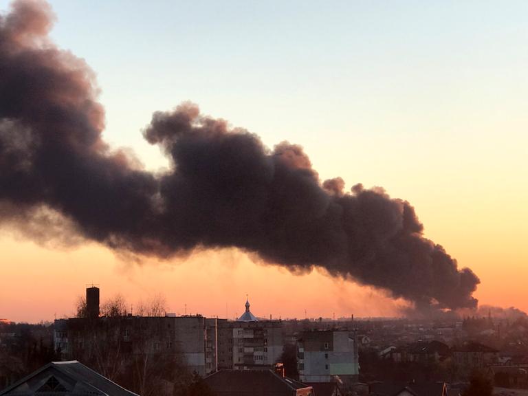 In der Dämmerung steicht eine dunkle Rauchsäule in einer Stadt auf. Es ist die ukrainische Stadt Lwiw.