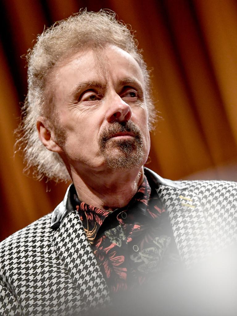 Porträt von T.C. Boyle. Er steht bei einer Veranstaltung auf einer Bühne vor einem Vorhang und trägt einen Blazer mit schwarzweißem Hahnentrittmuster.