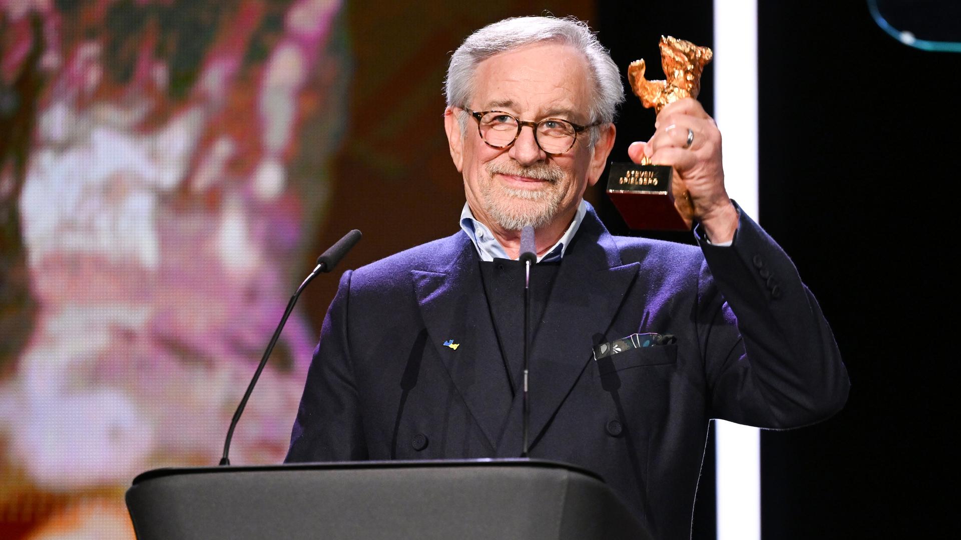 Steven Spielberg steht an einem Redner-Pult und hält den Goldenen Ehren-Bären hoch. Steven Spielberg steht an einem Redner-Pult und hält den Goldenen Ehren-Bären hoch.
