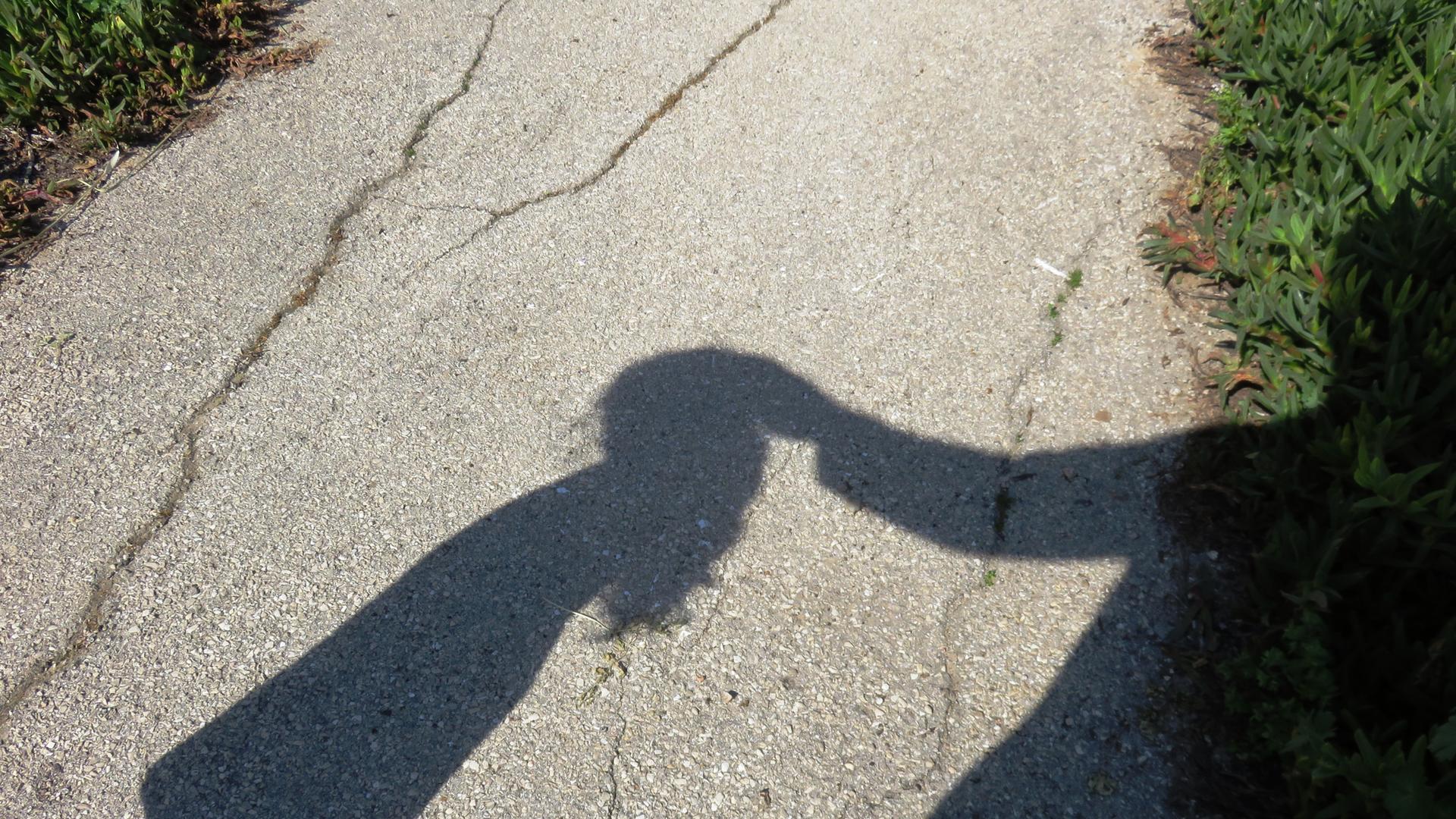 Der Schatten eines Kindes wird berührt von dem Schatten eines Erwachsenen. Der Schatten eines Kindes wird berührt von dem Schatten eines Erwachsenen.