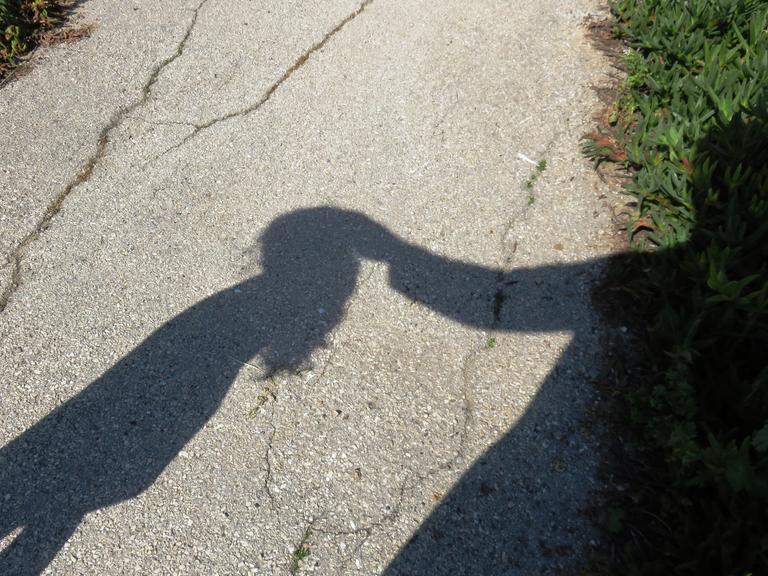 Der Schatten eines Kindes wird berührt von dem Schatten eines Erwachsenen.