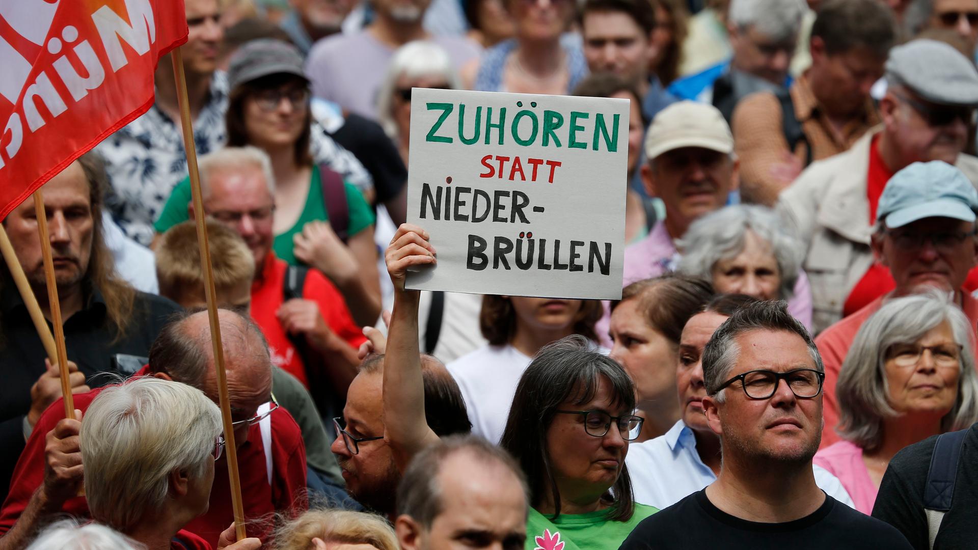 Demonstrierende mit einem Transparent mit der Aufschrift "Zuhören statt niederbrüllen" stehen am Münchner Odeonsplatz.