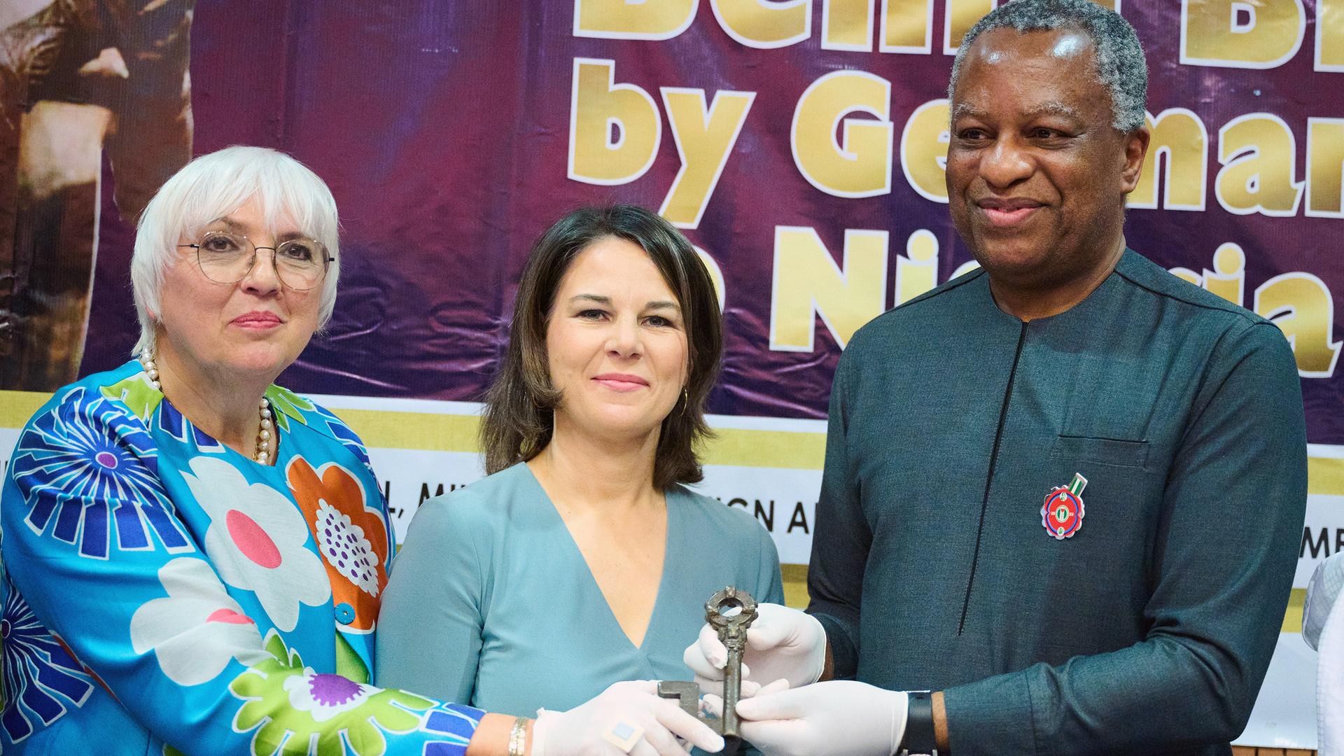 Das Foto zeigt Kultur-Staats-Ministerin Claudia Roth, Außen-Ministerin Annalena Baerbock und Geoffrey Onyeama, Außenminister von Nigeria. Alle drei halten gemeinsam eine Benin-Bronze in der Hand.