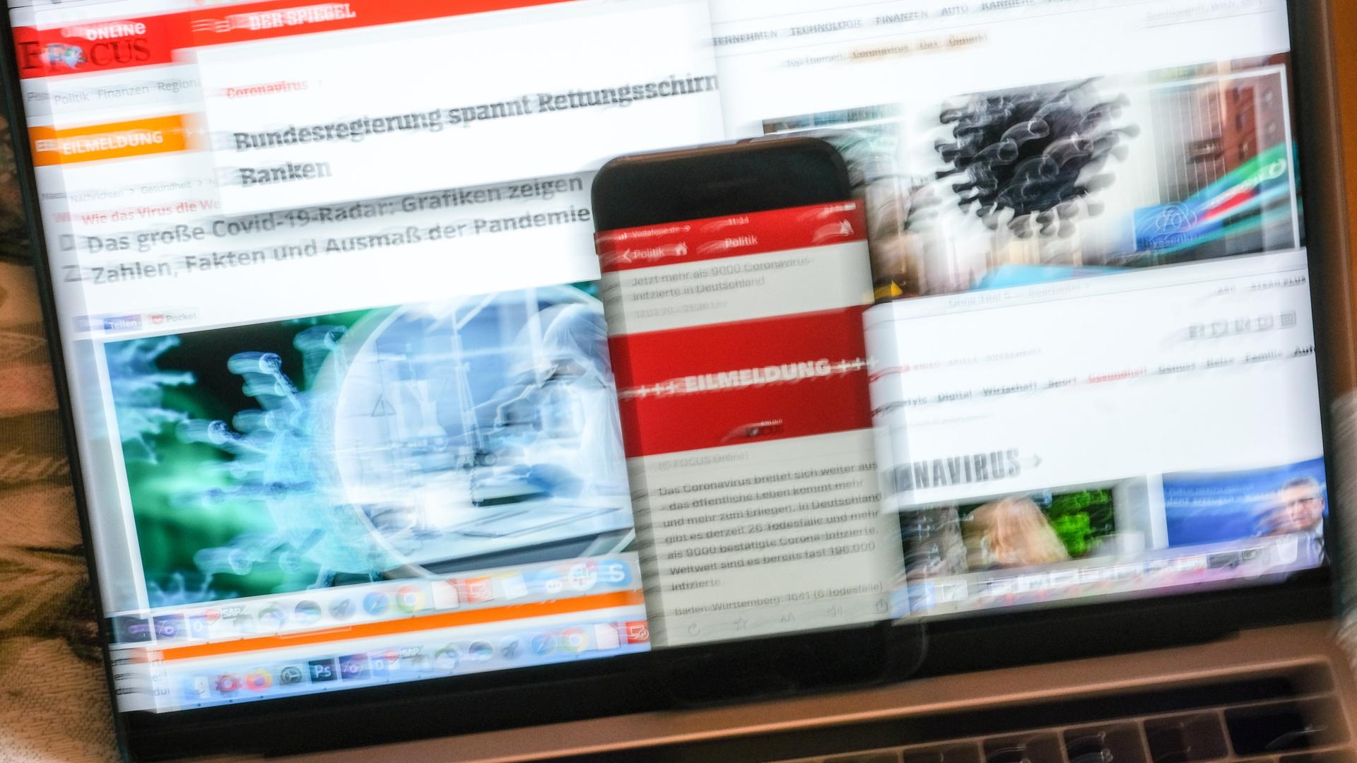 Auf einem Smartphone ist eine Eilmeldung eines Nachrichtenmagazins zur Corona-Krise angezeigt, das an einem Bildschirm mit Online-Angeboten von einigen überregionalen Zeitungen und Nachrichtenmagazinen steht. Auf einem Smartphone ist eine Eilmeldung eines Nachrichtenmagazins zur Corona-Krise angezeigt, das an einem Bildschirm mit Online-Angeboten von einigen überregionalen Zeitungen und Nachrichtenmagazinen steht.