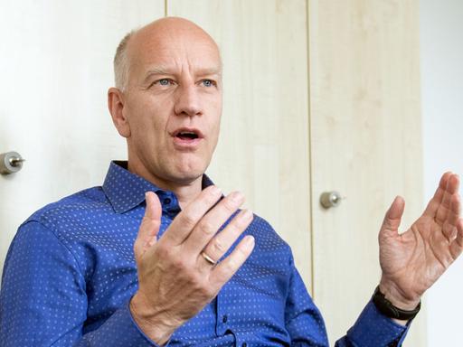 Ulf Dittmer, Leiter des Instituts für Virologie der Universitätsklinik, spricht während eines Interviews. Er sitzt auf einem Stuhl und trägt ein blaues Hemd. 
