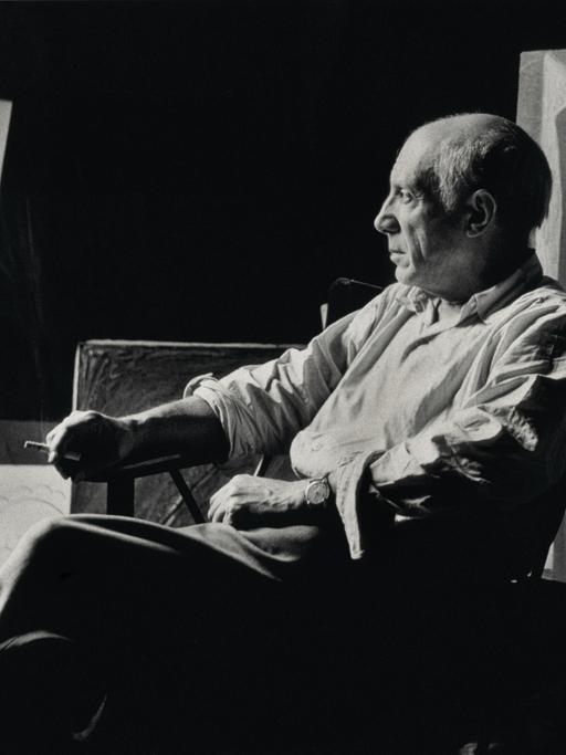 Pablo Picasso sitzt rauchend in seinem Atelier.