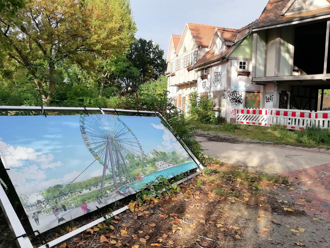 Auf dem Gelände des Spreeparks ist eine Illustration aufgestellt im Querformat in einem Rahmen gespannt und aufgestellt. Im Hintergrund sind Bäume und Häuser auf dem Gelände zu sehen, bei einem Haus fehlen ganze Wände. Auf dem Gelände des Spreeparks ist eine Illustration aufgestellt im Querformat in einem Rahmen gespannt und aufgestellt. Im Hintergrund sind Bäume und Häuser auf dem Gelände zu sehen, bei einem Haus fehlen ganze Wände.