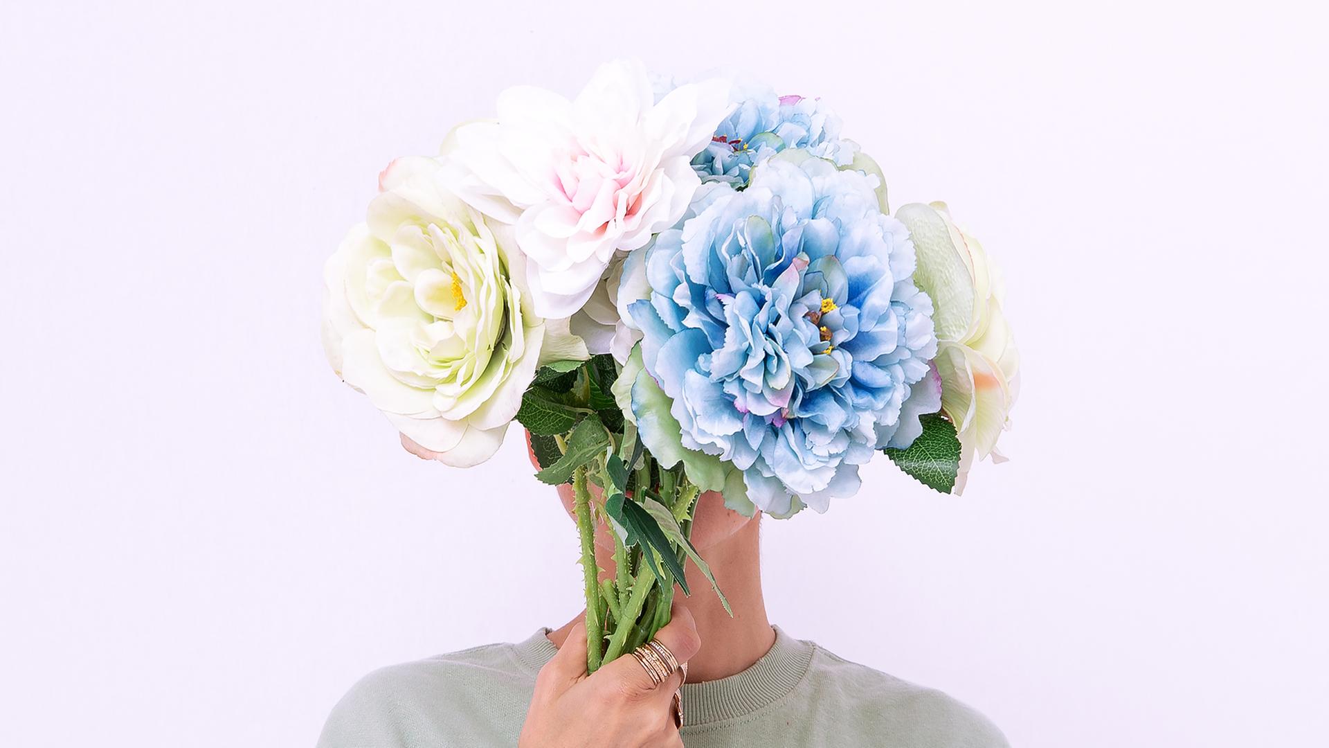 Eine Person verdeckt das Gesicht mit einem Blumenstrauß Eine Person verdeckt das Gesicht mit einem Blumenstrauß