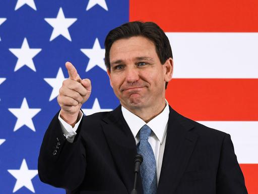 Der Gouverneur von Florida, Ron DeSantis, steht vor einer US-Flagge und zeigt nach vorne