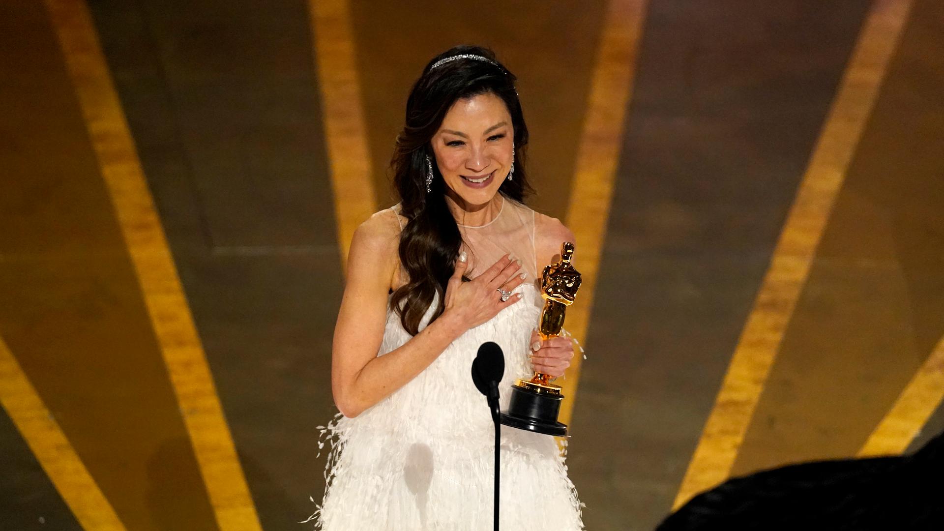 Die Schauspielerin Michelle Yeoh steht auf der Bühne der Oscar-Verleihung. In der Hand hält sie die Trophäe.