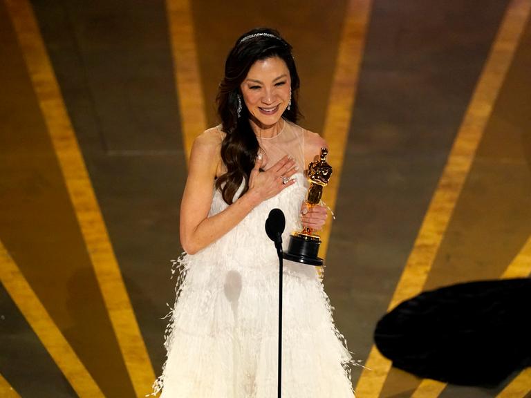Die Schauspielerin Michelle Yeoh steht auf der Bühne der Oscar-Verleihung. In der Hand hält sie die Trophäe.