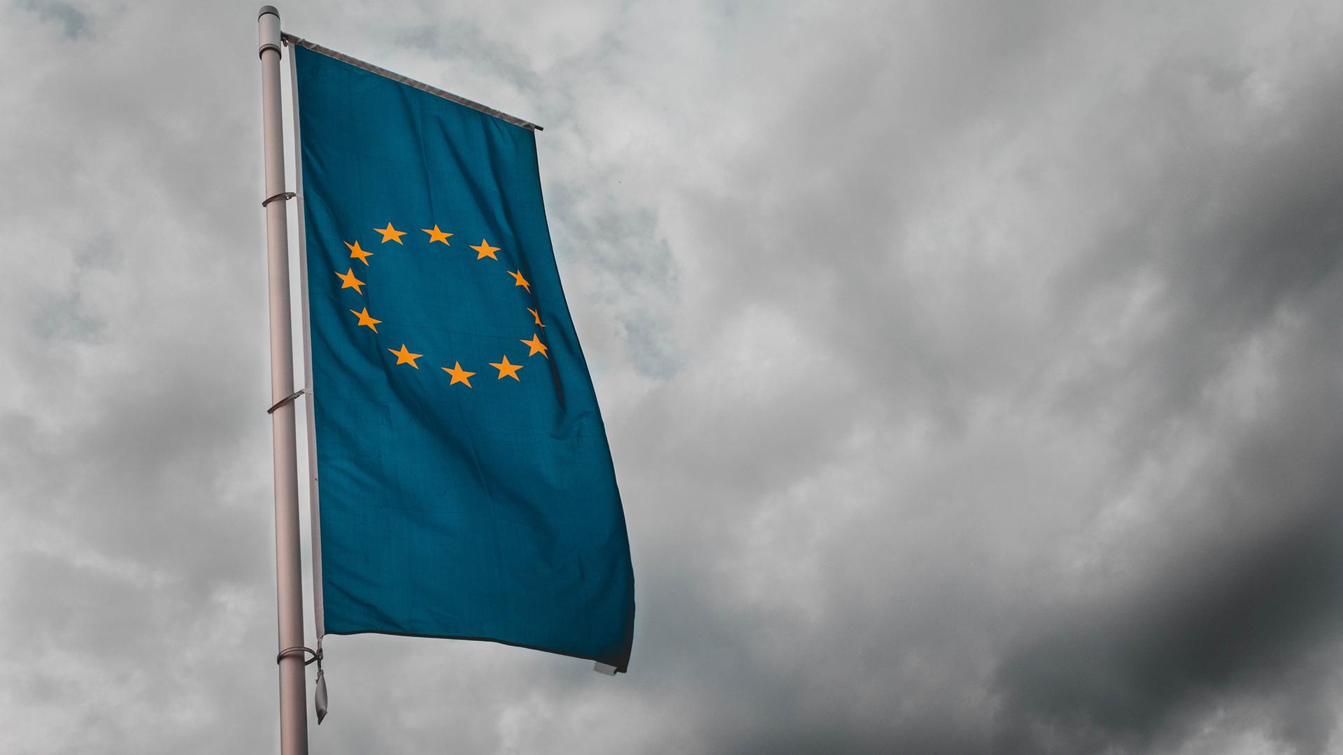 Eine Flagge mit den Sternen der Europäischen Union weht vor wolkenbedecktem Himmel.