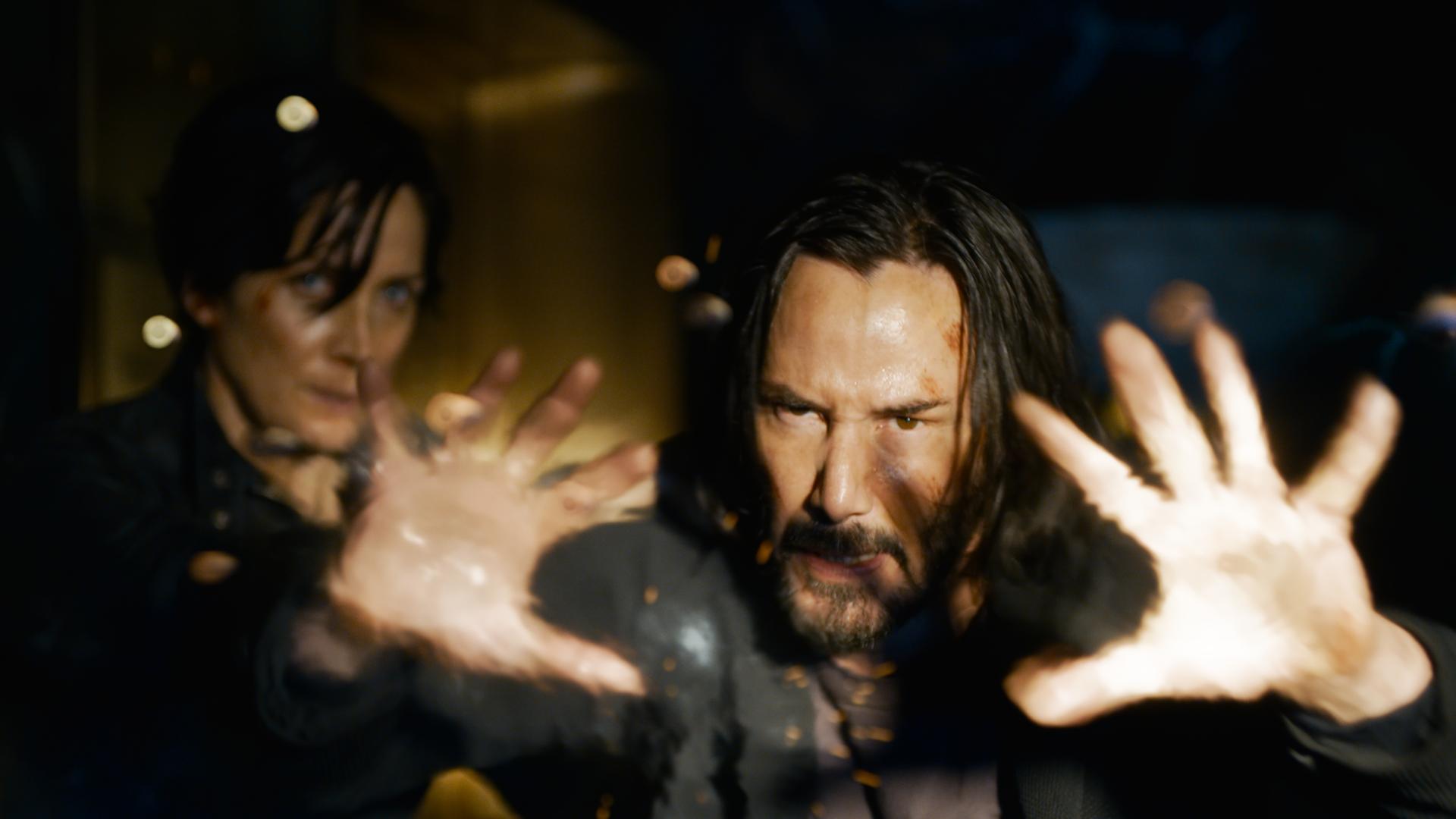 Keanu Reeves (Neo) und Carrie-Ann Moss (Trinity) in einer Szene des Films "Matrix Resurrections". Neo streckt die Hände einem unbekannten Gegner entgegen, Trinity blickt im Hintergrund furchtsam. Keanu Reeves (Neo) und Carrie-Ann Moss (Trinity) in einer Szene des Films "Matrix Resurrections". Neo streckt die Hände einem unbekannten Gegner entgegen, Trinity blickt im Hintergrund furchtsam.