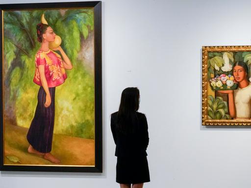Eine Frau steht vor Bildern des mexikanischen Malers Diego Rivera. 