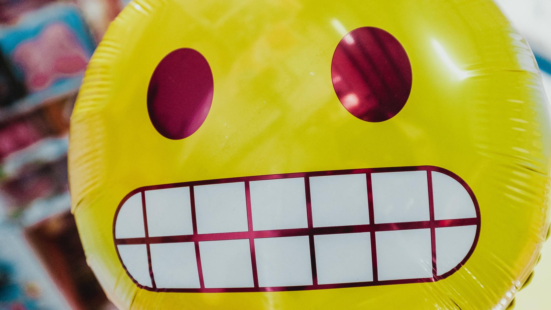 Ein runder gelber Ballon mit einem Emoji-Gesicht, das Zähne zeigt. Ein runder gelber Ballon mit einem Emoji-Gesicht, das Zähne zeigt.
