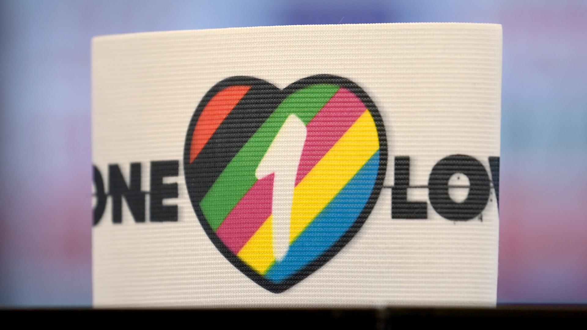 Die spezielle Kapitänsbinde als Zeichen gegen Diskriminierung und für Vielfalt liegt auf einem Tisch. Diese ziert ein Herz in bunten Farben, die für Vielfalt stehen, sowie die Aufschrift 'One Love'. Die spezielle Kapitänsbinde als Zeichen gegen Diskriminierung und für Vielfalt liegt auf einem Tisch. Diese ziert ein Herz in bunten Farben, die für Vielfalt stehen, sowie die Aufschrift 'One Love'.