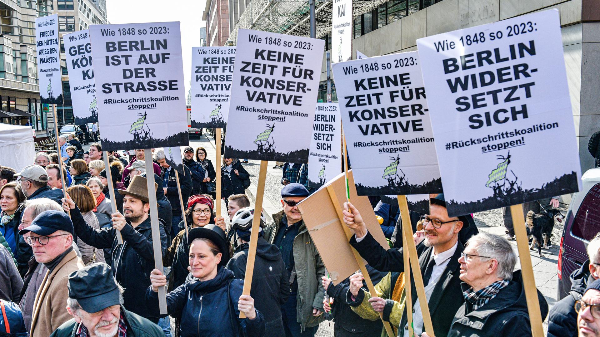 Demonstrierende tragen Schilder mit Aufschriften, die sich gegen die geplante Landesregierung aus CDU und SPD richten.